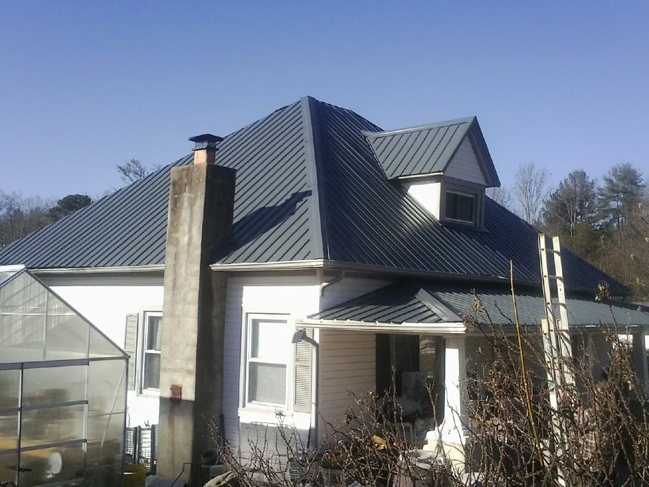 Dark blue standing seam metal roof on a white farmhouse with dormer — Slate & Tile Roof Repair by Roofing Brothers in Huntley