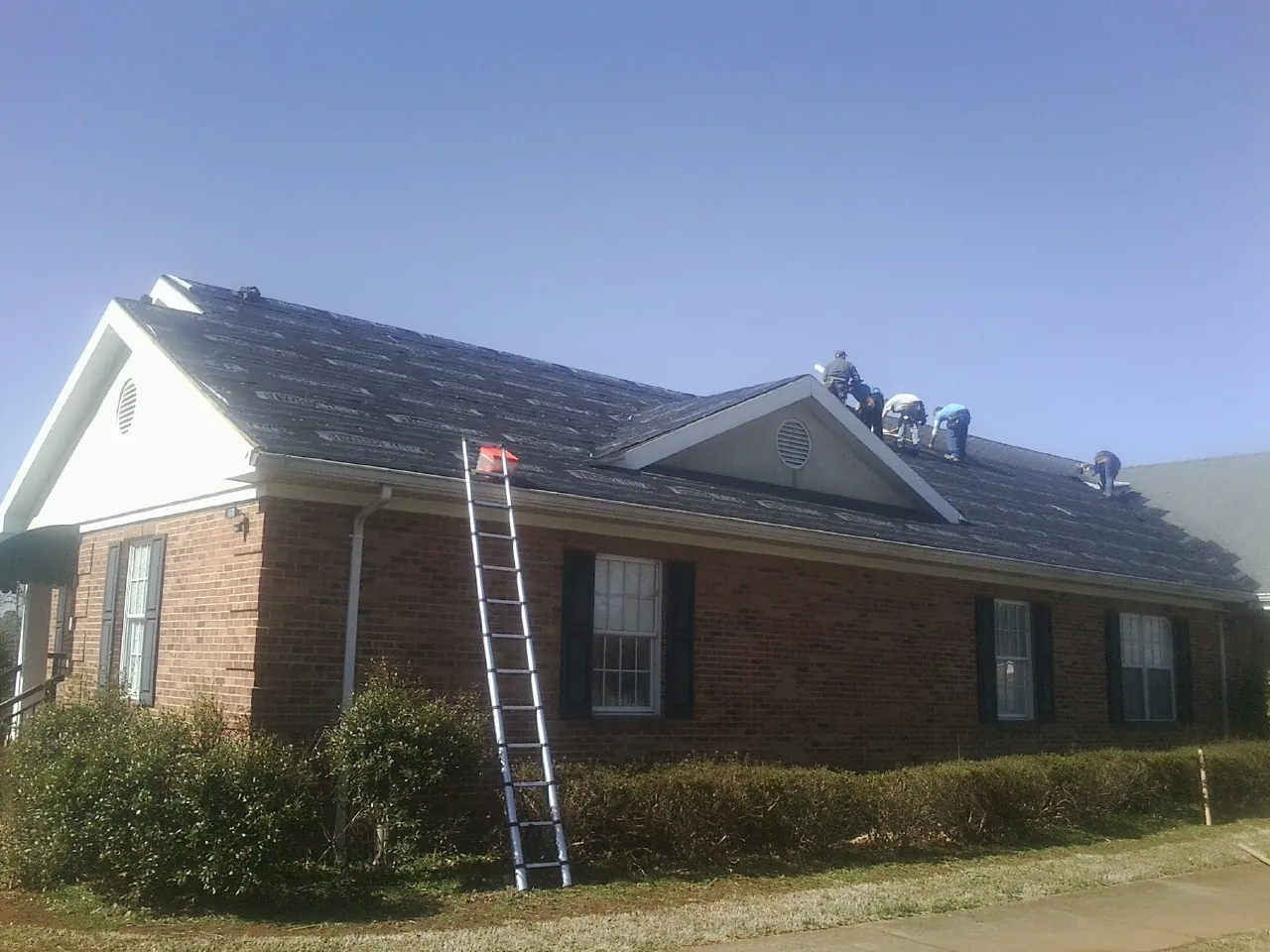 Crew tearing shingles off a brick ranch roof with a ladder set — Emergency Roof Repair work by our crew in Huntley