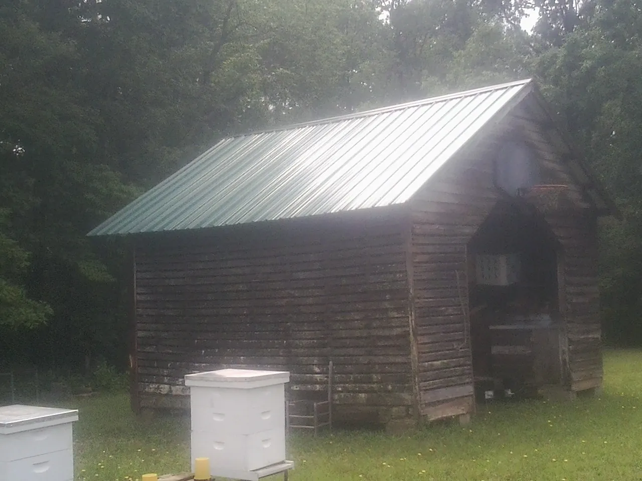 Green metal roof on a weathered barn beside stacked beehives in Huntley